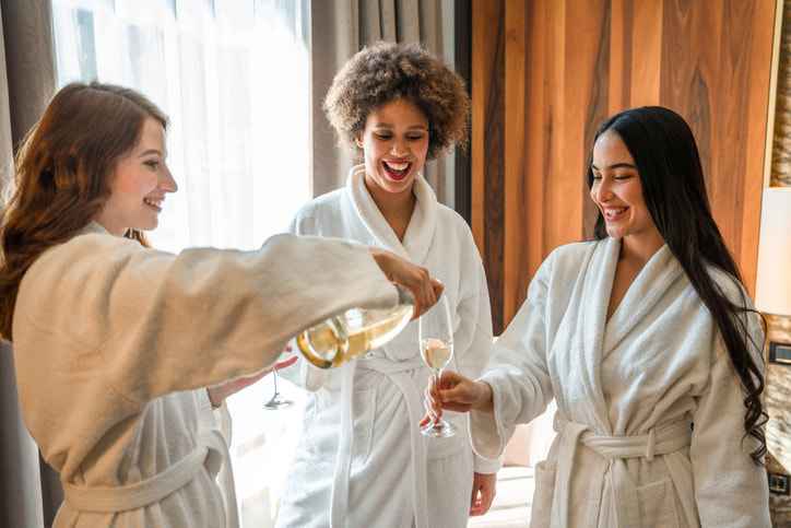 Women laughing, dancing and relaxing with a glass of sparkling wine at a spa