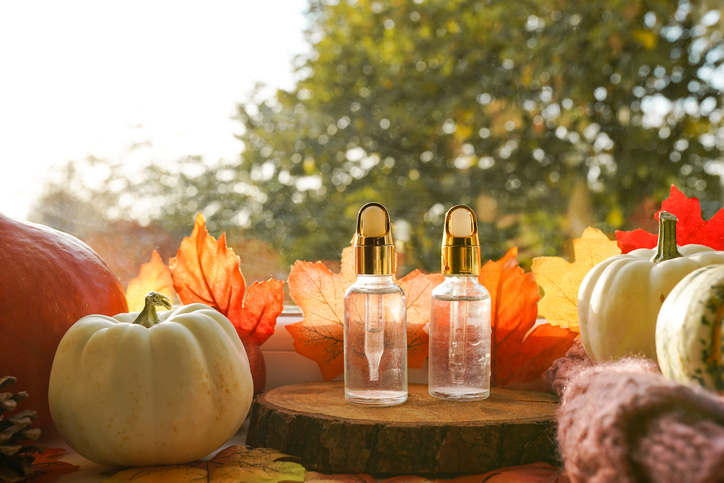 Transparent skincare bottles in ourdoor setting surrounded by leaves and pumpkins. Fall skincare concept